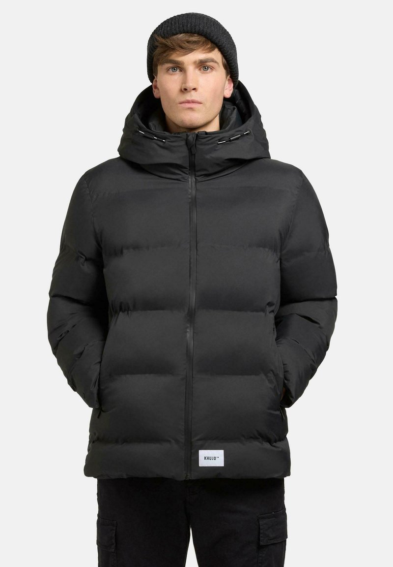 Schwarze gepolsterte Jacke mit Kapuze, ausgestattet mit einem Frontreißverschluss, seitlichen Taschen und einemLOGO-Patch am Saum. Glatte Textur und warmes Design.