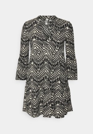 Robe tunique à manches longues noire et blanche avec un motif en zigzag, jupe à volants et col en V sur fond blanc.
