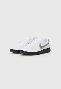 Sapatilhas brancas desportivas com parte superior têxtil, sola de borracha preta e swoosh cinza da Nike. Apresentam cordões planos e um design de bico arredondado.