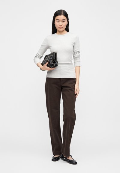 Világosszürke hosszú ujjú felső testhez simuló fazonnal, sötétbarna egyenes szárú nadrággal párosítva. A modell fekete, texturált borítéktáskát tart a kezében. Fekete lapos talpú cipő.