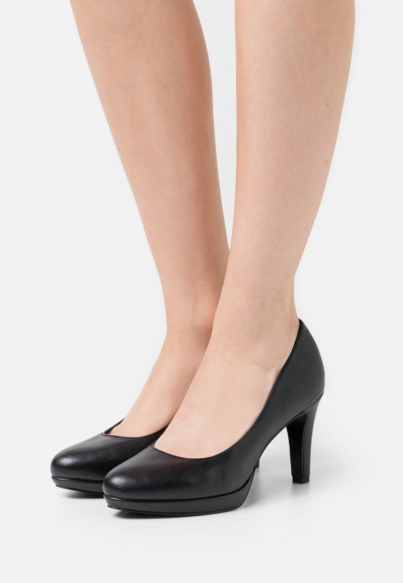 Chaussures à talons hauts en cuir noir avec un bout arrondi, présentant une texture lisse et une légère plateforme pour un ajout de hauteur.