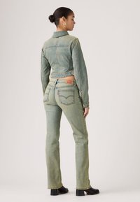 Σετ μπουφάν και τζιν παντελόνι σε ανοιχτό πράσινο. Κοντό μπουφάν με κλείσιμο με κουμπιά· παντελόνι ψηλόμεσο με παραδοσιακές πίσω τσέπες και σήμανση.