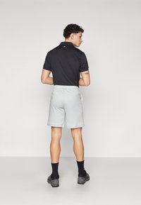 Fekete póló, rövid ujjú, világosszürke rövidnadrággal párosítva. A rövidnadrág elasztikus derékpánttal és oldalsó zsebekkel rendelkezik. Fekete zokni és cipő.