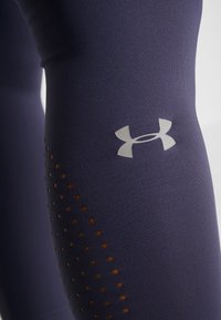 Navy leggings made of stretchy fabric, featuring a silver logo and a side panel with brown perforations for ventilation.