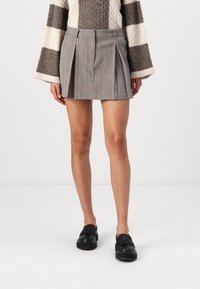 Grå rutete mini skjørt med legg, flat liv, og skreddersydd design. Kombinert med svarte kraftige sko og en teksturert genser.