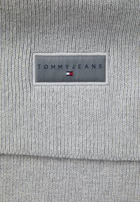 Gray ribbed knit fabric with a rectangular woven label displaying "TOMMY JEANS" and a small red, white, and blue logo underneath.