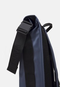 Gros plan sur un sac à dos bleu avec un dos en maille rembourrée et une large sangle noire réglable dotée d'une boucle en plastique.