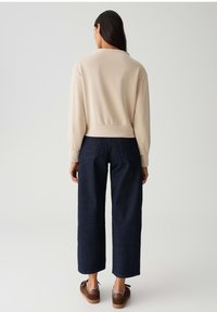 Felpa beige con un design cropped e polsini a costine, abbinata a pantaloni in denim a gamba larga di un blu scuro. Caratterizzata da uno stile pulito e minimalista.