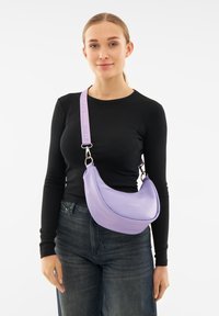 Lila hobo-laukku, joka on valmistettu sileästä materiaalista. Laukussa on kaareva muoto, säädettävä olkahihna ja huomaamaton merkintä painettuna etupuolelle.