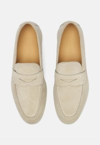Mocassini in suede beige con tomaia cucita, forma liscia e un flap decorativo. La fodera interna è color tan e presenta un'elegante impuntura con logo in rilievo.