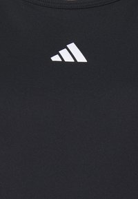 T-shirt de sport noir avec une texture lisse, arborant un logo Adidas blanc en design triangulaire sur le devant.