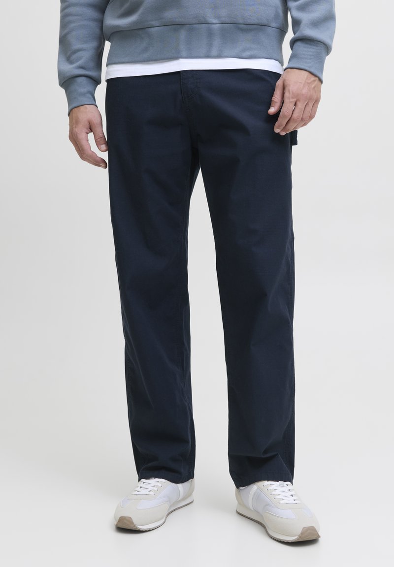 Pantaloni in cotone blu navale con design a gamba dritta, dotati di tasche laterali e una texture liscia, abbinati a sneakers bianche.