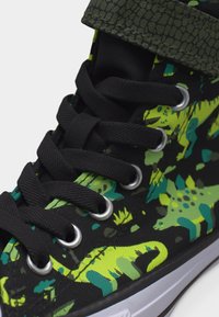 Μαύρο αθλητικό παπούτσι υψηλής κορυφής με φωτεινά πράσινα και μπλε μοτίβα δεινοσαύρων, μαύρα κορδόνια, μεταλλικά υφάσματα και υφασμάτινο πράσινο λουρίστο στο περιλαίμιο.