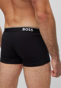 Črne boksarice z elastičnim pasom, ki imajo napis blagovne znamke "BOSS" v belih črkah; gladek material z oprijetim krojem.