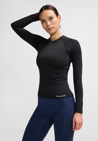 Schwarzes Longsleeve-Athletic-Shirt aus strukturiertem Stoff mit Logo am Saum, kombiniert mit navyblauen Leggings mit glatter Oberfläche.