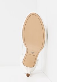 Bílá dámská lodička na vysokém podpatku, pohled zespodu, s hladkým bílým svrškem, světlou podrážkou a špičatou špičkou. Na podrážce je logo značky.