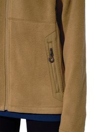 Beige fleecejas met een rits aan de voorkant en een verticale ritssluiting aan de zijkant, gedragen over een blauw kledingstuk en een zwarte broek.