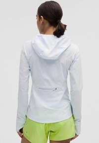 White lightweight jacket with a hood, featuring a zippered back pocket and fitted design. Paired with bright green shorts. Smooth texture.