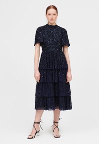 Vestido de color azul marino con volantes y mangas cortas, adornado con lentejuelas, que presenta un escote redondo y una silueta texturizada y fluida.