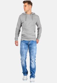 Grijze hoodie met een voorzak en verstelbare koordjes, gecombineerd met lichtblauwe spijkerbroek en witte sneakers.