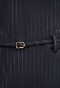Tissu bleu marine à fines rayures avec une ceinture fine assortie et une petite boucle rectangulaire dorée.