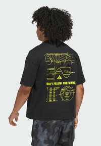 Zwarte T-shirt met een groot geel grafisch ontwerp op de achterkant, met golfpatronen en wetenschappelijke tekst. Korte mouwen, relaxte pasvorm.