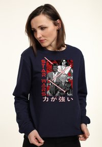 Mörkblå sweatshirt med ett grafiskt tryck av tre karaktärer från Star Wars, omgivna av rött med japansk text nedanför. Tillverkad i bomull.