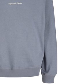 Ανοιχτό μπλε φούτερ με ριμπ τελείωμα και μανσέτες, με λευκό κείμενο με καλλιγραφική γραμματοσειρά "Originals Studio" κοντά στον λαιμό.