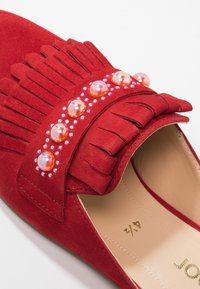 Chaussure plate en daim rouge avec détail de franges, perles décoratives et strass le long de la bande supérieure. Intérieur de couleur beige clair. Taille indiquée : 42.