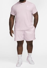 T-shirt rose Nike et short assorti en tissu doux. Présente un petit logo blanc sur le T-shirt. Porté avec des baskets et des chaussettes blanches.