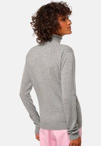 Pull en col roulé gris en matière tricotée douce ; coupe ajustée avec des manches longues et un col et des poignets côtelés.