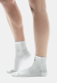 Weiße Sportsocken mit geripptem Muster, die eine Kombination aus festen und Netzbereichen aufweisen. Enthält ein Logo in der Nähe des Knöchels und verstärkte Fersen.