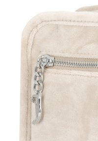 Angolo di una borsa in velluto beige con cerniera argentata, tirante a catena e texture morbida. Presenta una cucitura visibile e un accento metallico lucido.