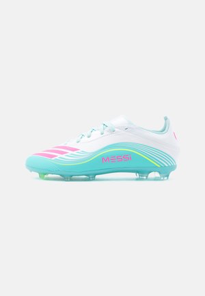 Botas de fútbol blancas y turquesas con detalles en rosa, marca "MESSi" y tacos moldeados para jugar en campo firme.