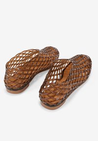 Zapatos marrones de punta abierta y tipo slip-on, hechos de un material plástico tejido. El diseño presenta un patrón entrelazado y un forro interior suave.