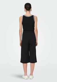 Svart byxdress med tajt överdel och vida culotterben. Har vit kant längs halsringningen. Tillverkad av mjukt, elastiskt tyg.