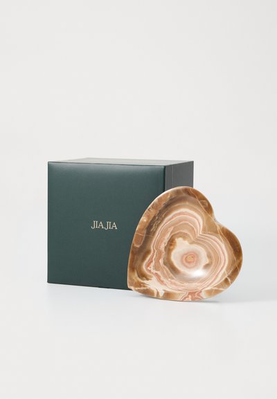 Vas cu formă de inimă din onix în tonuri calde de crem și roz, având modele naturale ondulate, așezată lângă o cutie de ambalaj de culoare verde închis.