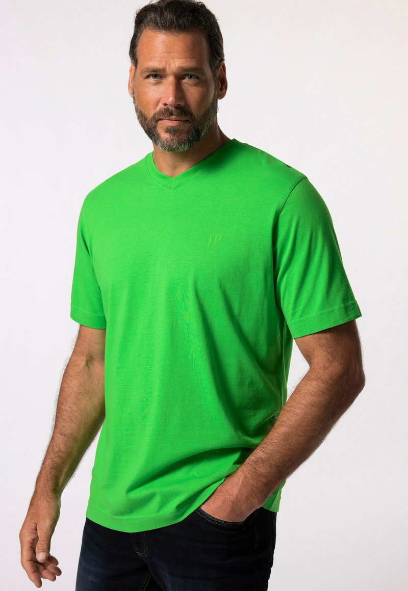 Camiseta verde claro de manga corta y escote en V hecha de suave algodón. Presenta un logo sutil en la esquina superior izquierda, combinada con jeans oscuros.