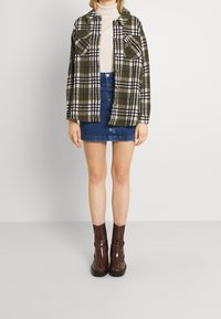 Zeleno-bílá kára flanelová košile s dvěma náprsními kapsami přes béžový rolák, který je doplněn modrou džínsovou minisukní a hnědými kotníkovými botami.