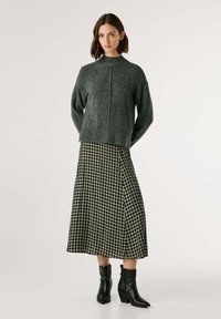 Suéter de malha cinza-escuro com gola alta, combinado com uma saia midi de xadrez preto e branco e botas de tornozelo pretas.