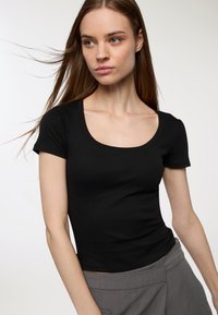 Czarny prążkowany t-shirt z okrągłym dekoltem i krótkimi rękawami, dopasowany krój, noszony z szarymi spodniami o wysokim stanie. Gładka tekstura i minimalne detale.