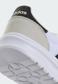 Sneaker blanche avec des accents en daim gris et un talon en cuir noir. Présente une semelle en caoutchouc texturée avec le logo "CLOUDFOAM".