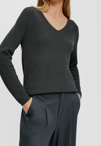 Dunkelgrauer gerippter Strickpullover mit V-Ausschnitt, langen Ärmeln und lässiger Passform, kombiniert mit dunklen grauen, maßgeschneiderten Hosen mit Seitentaschen.