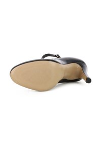 Scarpa con tacco alto in vernice nera, dalla forma affusolata e con un piccolo cinturino alla caviglia. La suola è beige e presenta linee di grip testurizzate.
