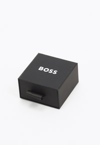 Scatola quadrata nera con un'etichetta di trazione, con la parola "BOSS" stampata in bianco sulla parte superiore. Realizzata in materiale di cartone liscio.