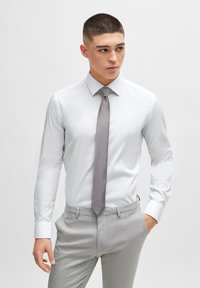 White dress shirt with a pointed collar, paired with a grey striped tie and light grey patterned trousers. Smooth fabric, tailored fit.