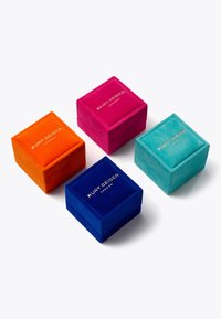 Quattro scatole di gioielli in velluto di colore arancione, rosa, blu e verde acqua, con lettering dorato. Ogni scatola ha una forma quadrata e una texture morbida.