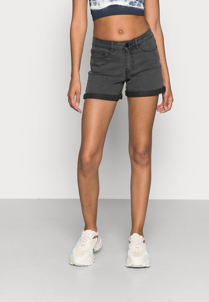 Svart denimshorts med upprullade fållar, femficksdesign, knäppning med knapp, matchade med ljusa sneakers och en kort, batikfärgad topp.
