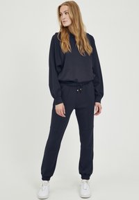 Mörkblå hoodie och matchande joggers i mjukt material. Hoodien har en lös passform och dragsnören; joggersen har elastiska fållar och sidofickor.