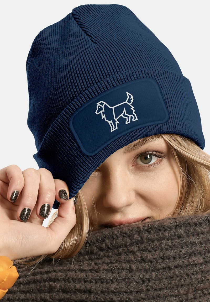 Navy knit beanie with a ribbed texture, featuring a central patch with a white outline of a dog. Warm, flexible material for comfort.